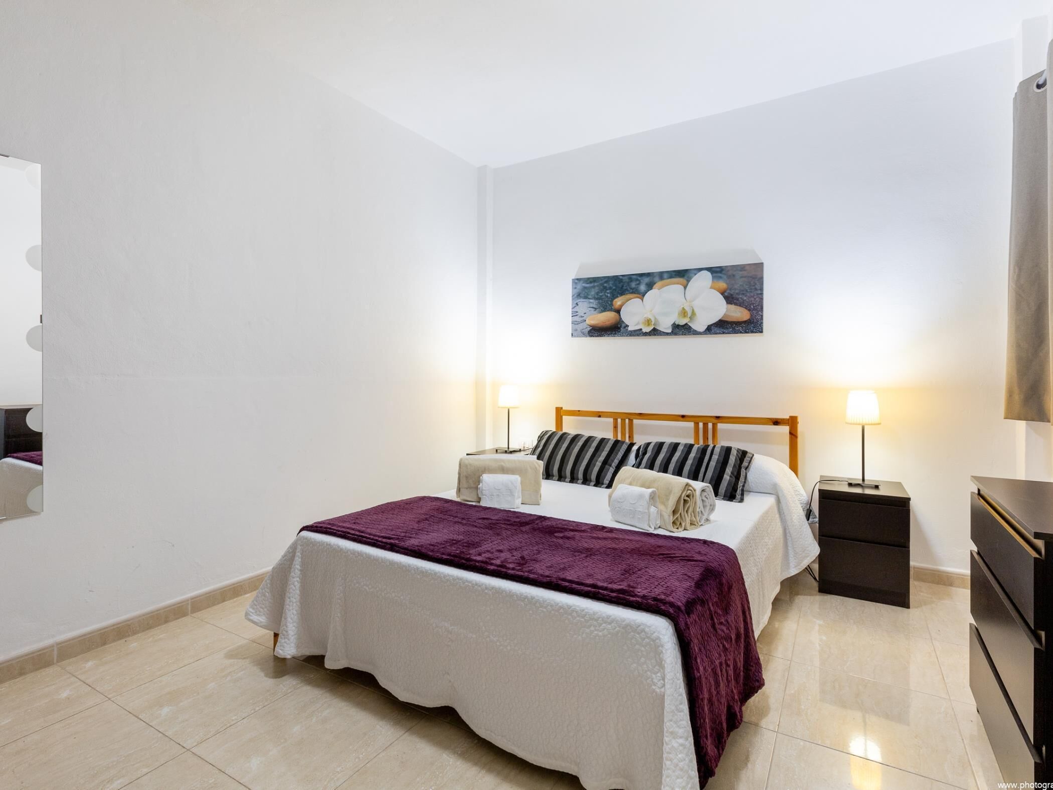 Una habitación de hotel con cama, mesitas de noche, lámpara y un cuadro en la pared.