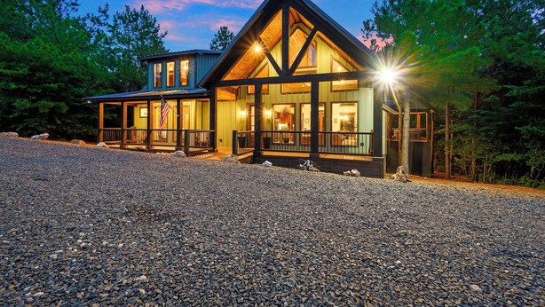 A modern log cabin with a large deck and a prominent American flag. - Broken Bow Home w/ Hot Tub, Game Room & EV Charger (Broken Bow)