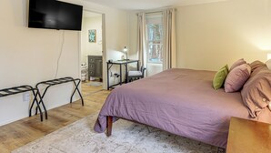 Un dormitorio con una cama grande, un televisor de pantalla plana en la pared, un escritorio con una silla y una ventana con cortinas.