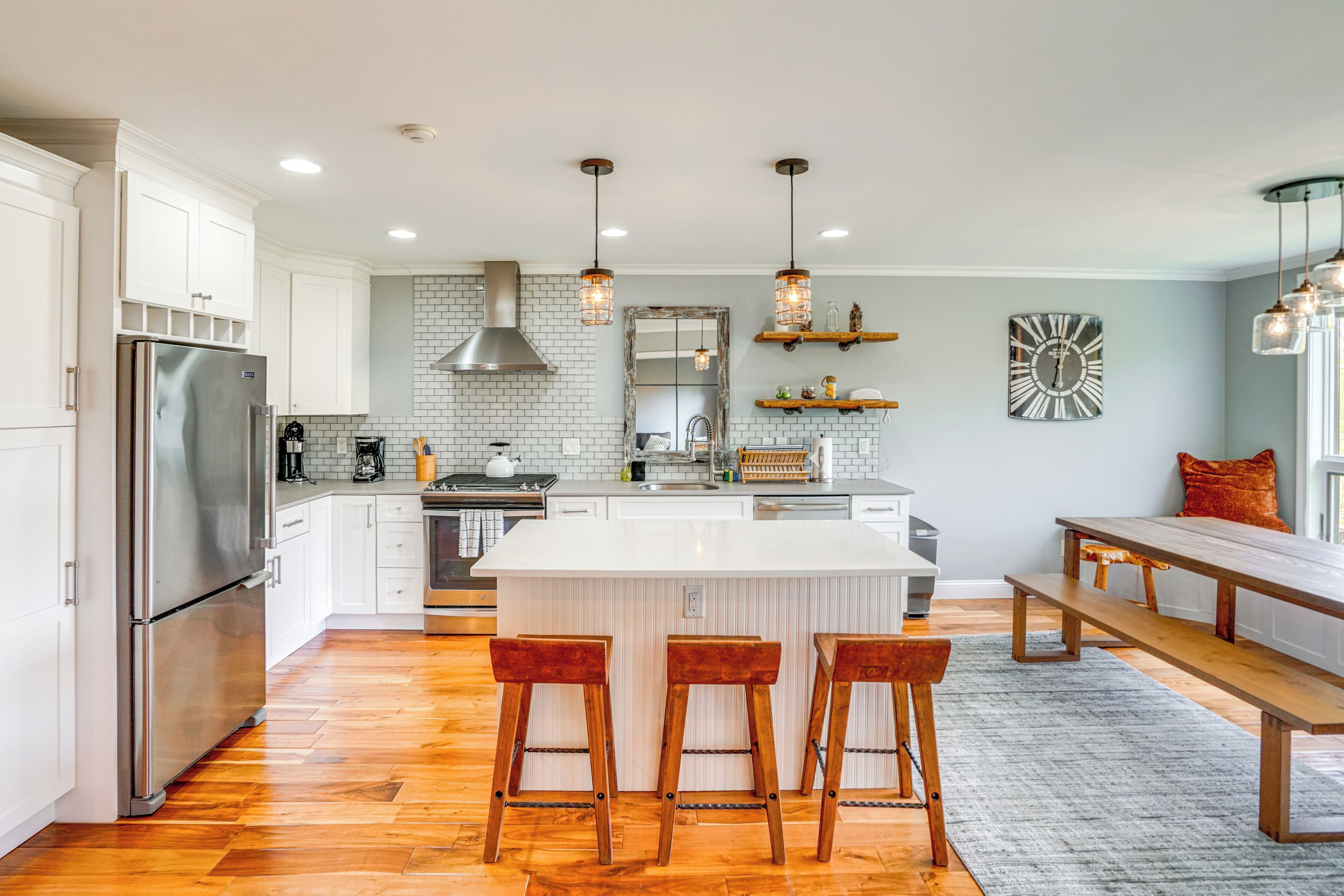 A modern kitchen with white cabinetry, a stainless steel refrigerator, wooden stools, and pendant lighting.