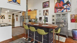 A modern kitchen with a central island, bar stools, and various artworks on the walls. - Chic Loft Retreat blocks from the Quarter! (New Orleans)