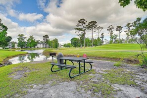 Een picknicktafel met banken en een vuilnisbak in een park met een vijver en bomen.