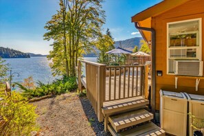 Eine Holzterrasse mit Stufen zu einem überdachten Außenbereich, mit Blick auf einen See, Bäume und Hügel im Hintergrund.