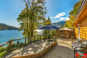 A wooden deck with outdoor furniture, a pergola, and a view of a lake and mountains.