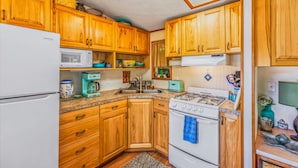 A compact kitchen with wooden cabinets, a white refrigerator, a microwave, a stove, and a coffee maker. - Reed s Cove Cabin in Hoodsport (Hoodsport)
