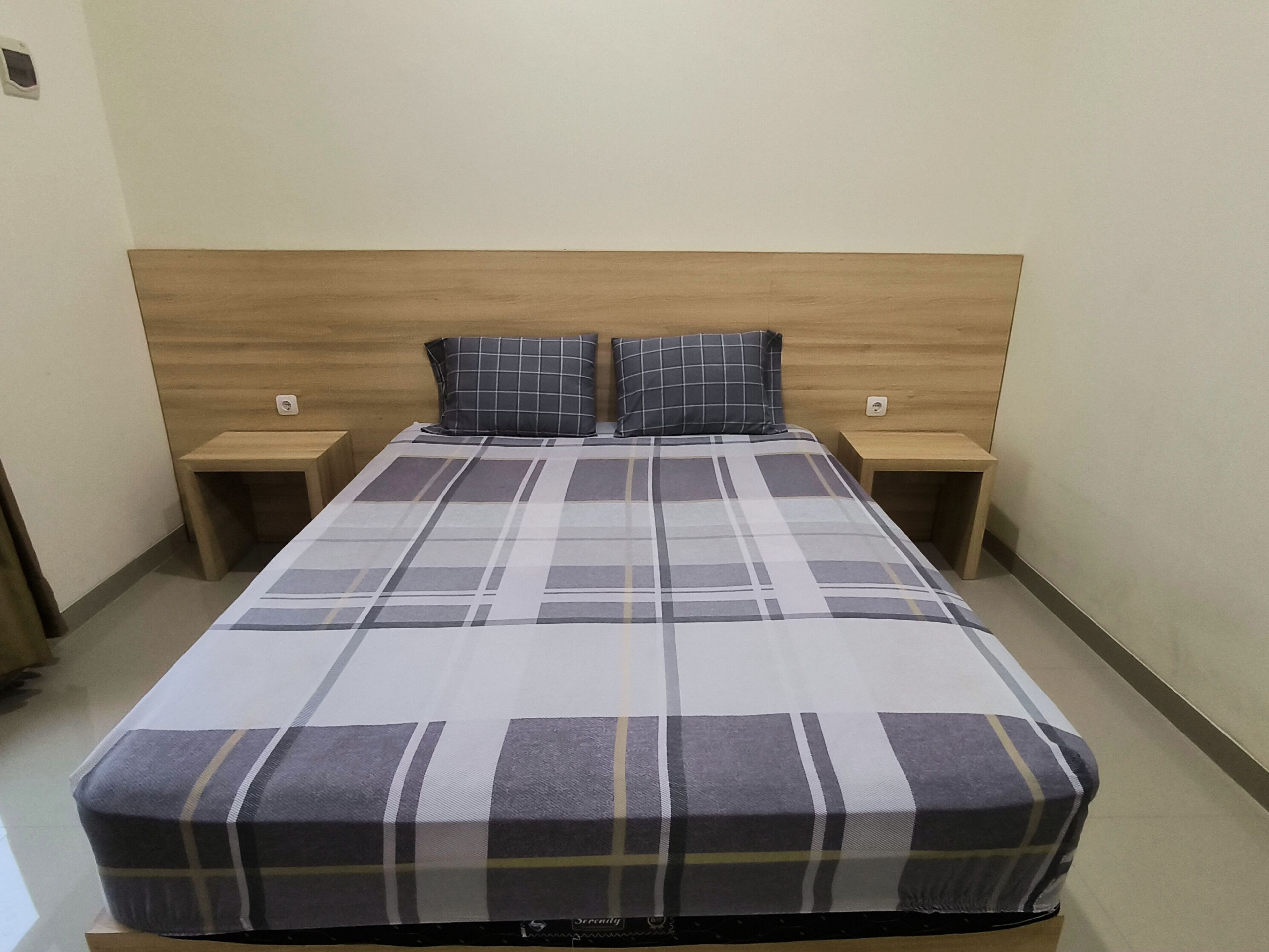 A neatly made bed with a plaid bedspread, two pillows, and two bedside tables with lamps.