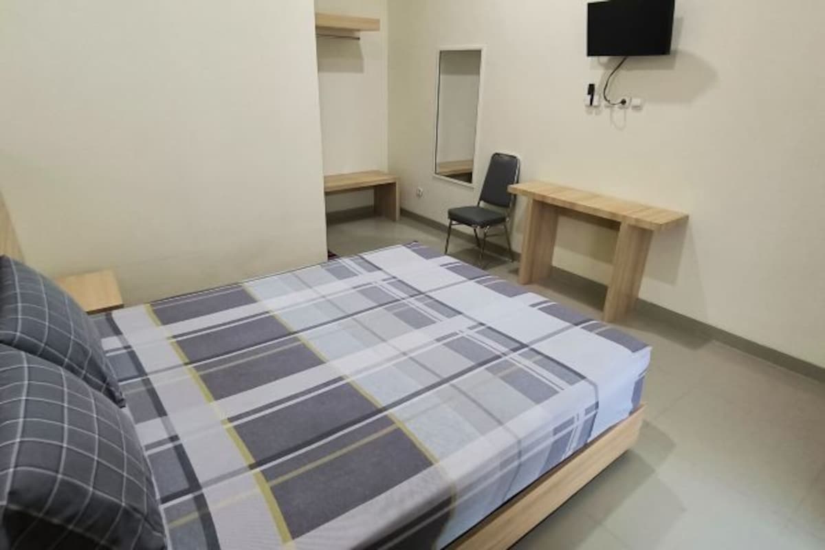 A bedroom with a bed, a desk, a chair, a TV, and a mirror.