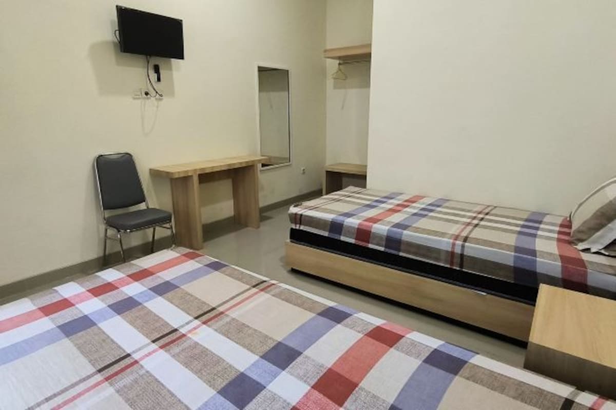 A bedroom with two beds, a desk, a chair, a television, and a mirror.