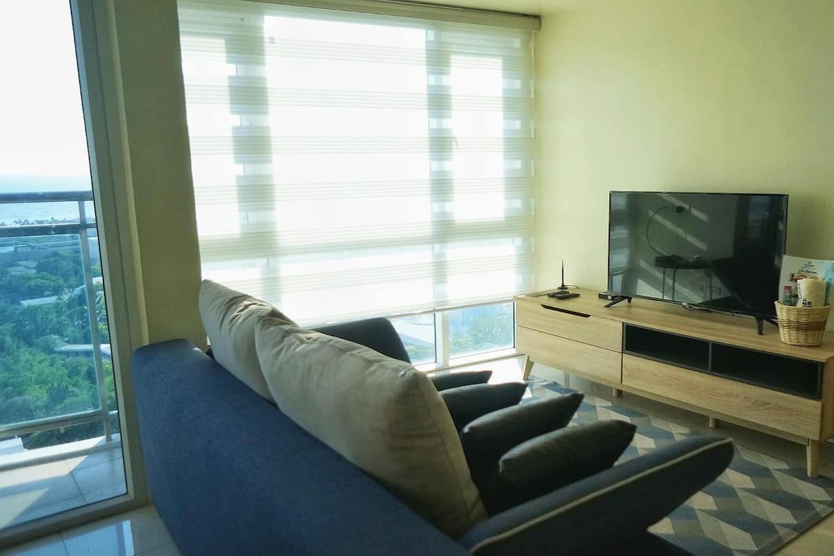 Ein modernes Wohnzimmer mit großem Fenster, einer Couch, einem Fernseher und einer Holzkabine.