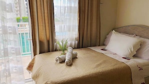 Een hotelkamer met een bed, een kamerplant en uitzicht op een gebouw en groen buiten.