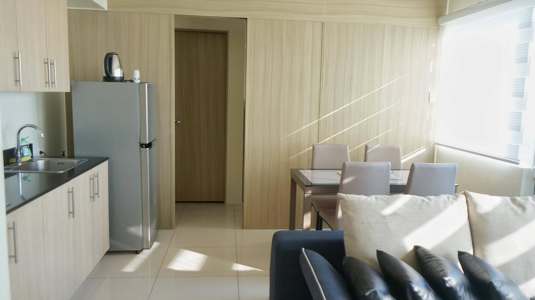 A compact kitchen with a refrigerator, sink, and kettle, leading to a dining area with a table and chairs.