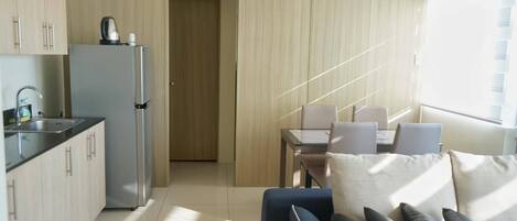A compact kitchen with a refrigerator, sink, and kettle, leading to a dining area with a table and chairs.