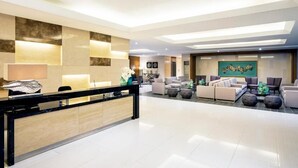Een moderne hotellobby met een receptiebalie, een zithoek en kunstwerken aan de muren.