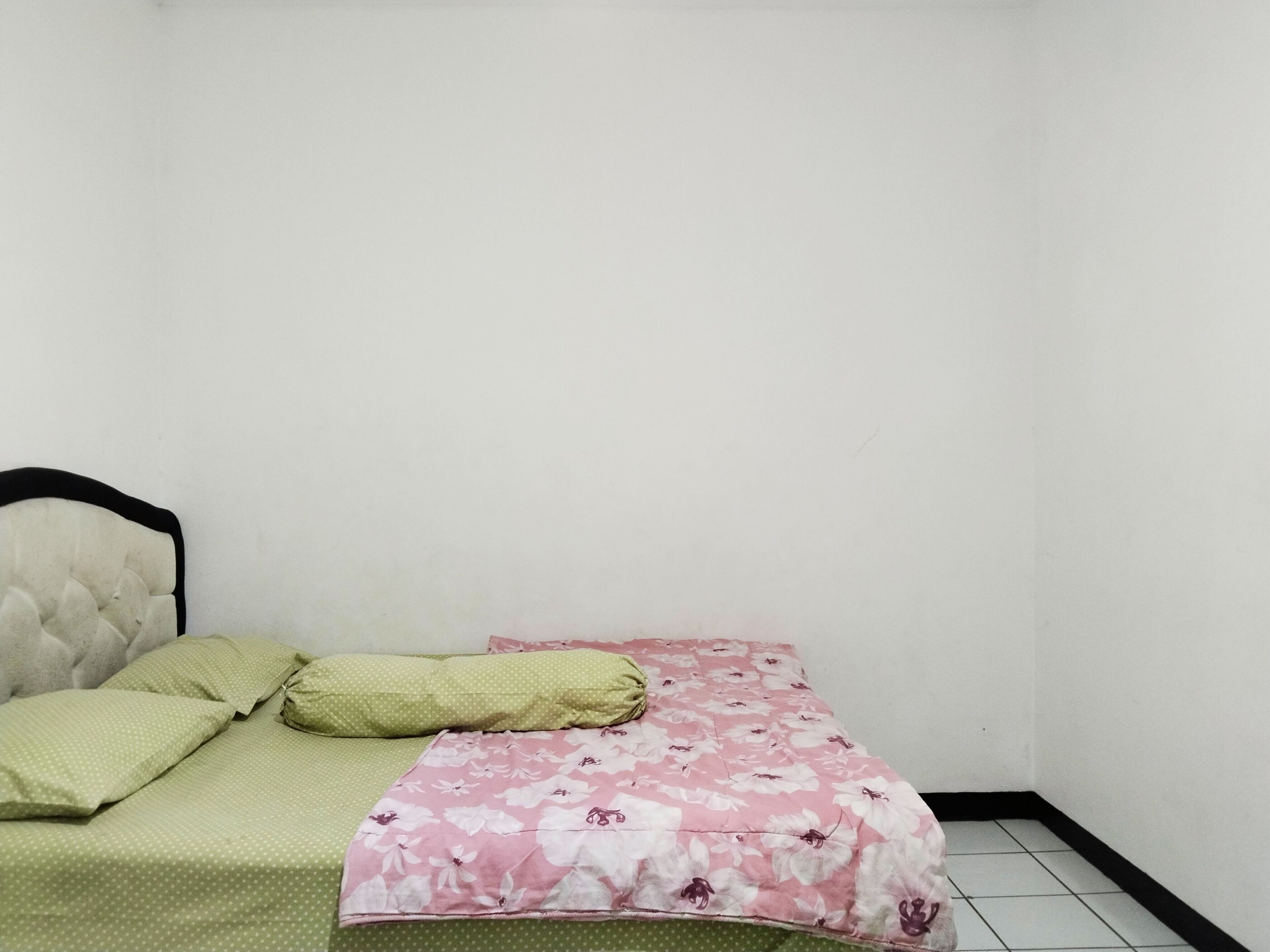 Una habitación pequeña con cama individual, colcha estampada, almohada verde y cabecera.
