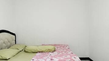 Una habitación pequeña con cama individual, colcha estampada, almohada verde y cabecera.
