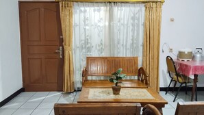 A dining area with a wooden table, chairs, a potted plant, and a table with a kettle and a container. - Villa Estria (Cisarua)
