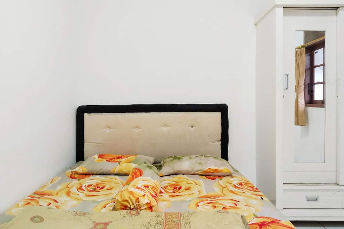 Una cama con ropa de cama estampada, cabecera capitonada y un armario blanco con espejo.