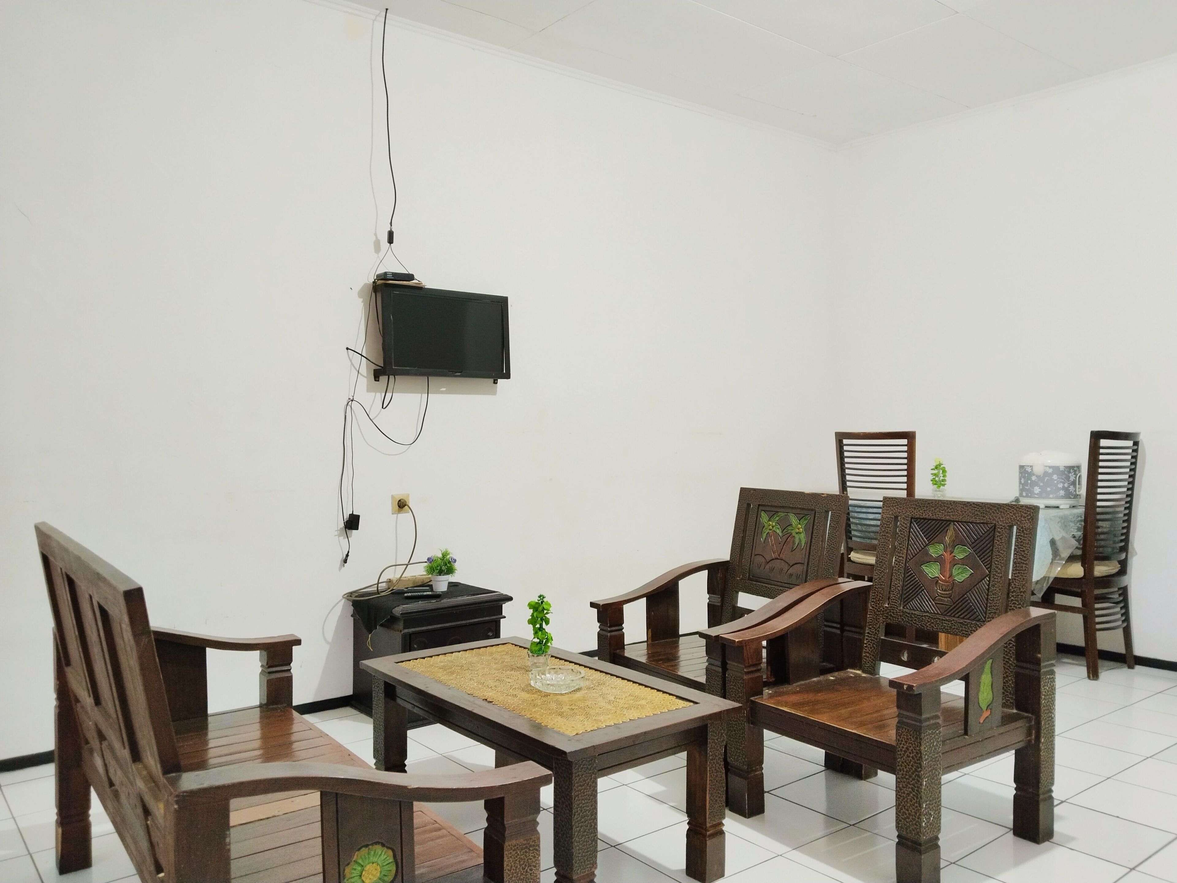 A room with a wooden dining table, four wooden chairs, a television mounted on the wall, and a small black cabinet.