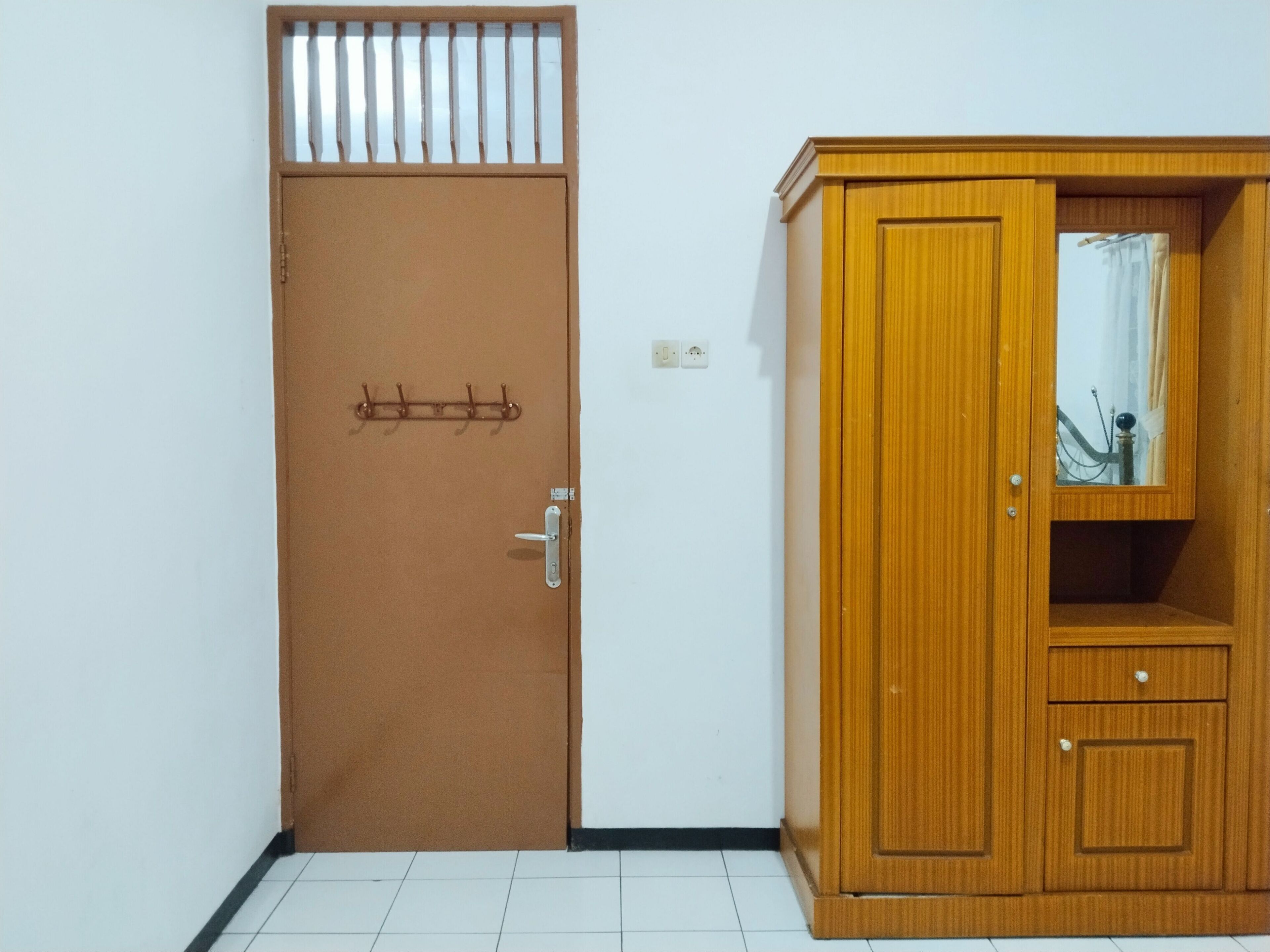 Una habitación con una puerta marrón, un armario de madera con espejo y suelo de baldosas.