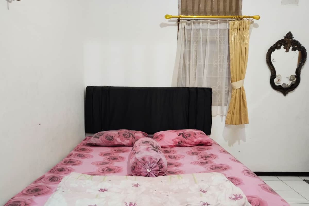Una cama con colcha floral, cabecera negra y almohada decorativa.