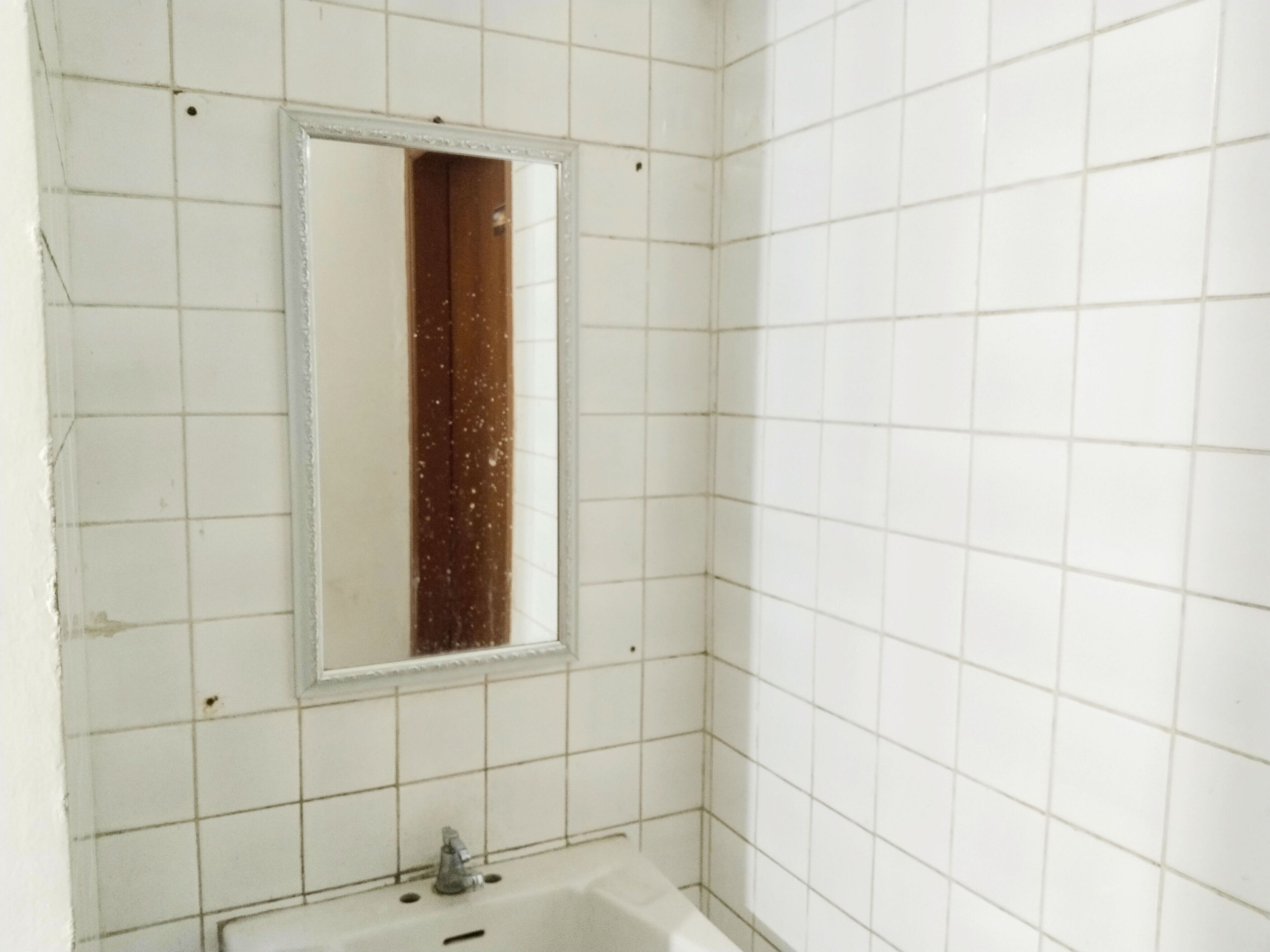 Ein Badezimmer mit weißen Fliesen, einem Spiegel und einem Waschbecken.