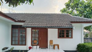 A house with a tiled roof, a front door, two windows, a small porch, and a set of steps leading to the door. - Villa Estria (Cisarua)