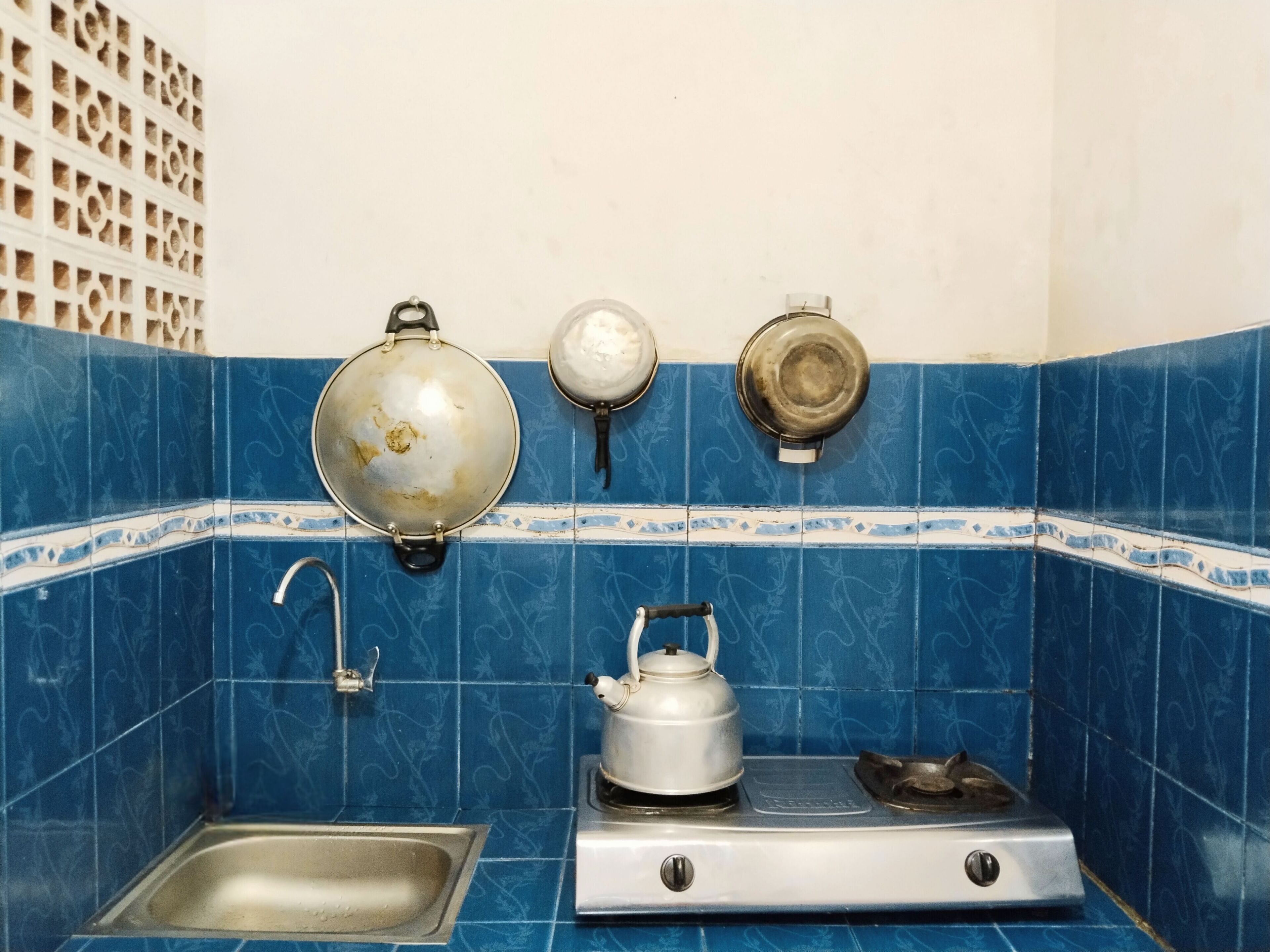 A kitchen with blue patterned tiles, a stainless steel sink, a kettle, and a stove.