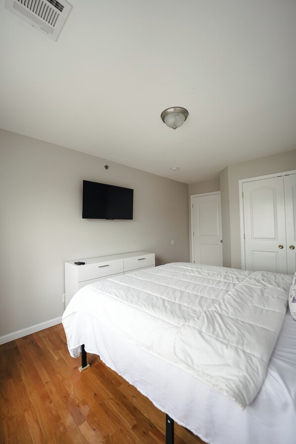 A bedroom with a bed, a flat-screen TV mounted on the wall, a white wardrobe, and a door.