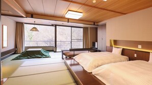 Une chambre d’hôtel avec deux lits, un canapé, une télévision et une grande fenêtre donnant sur la verdure.