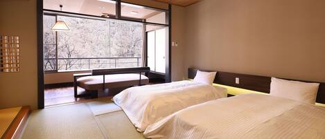 A hotel room with two beds, a bench, a window with a view of trees, and a traditional Japanese tatami mat floor.