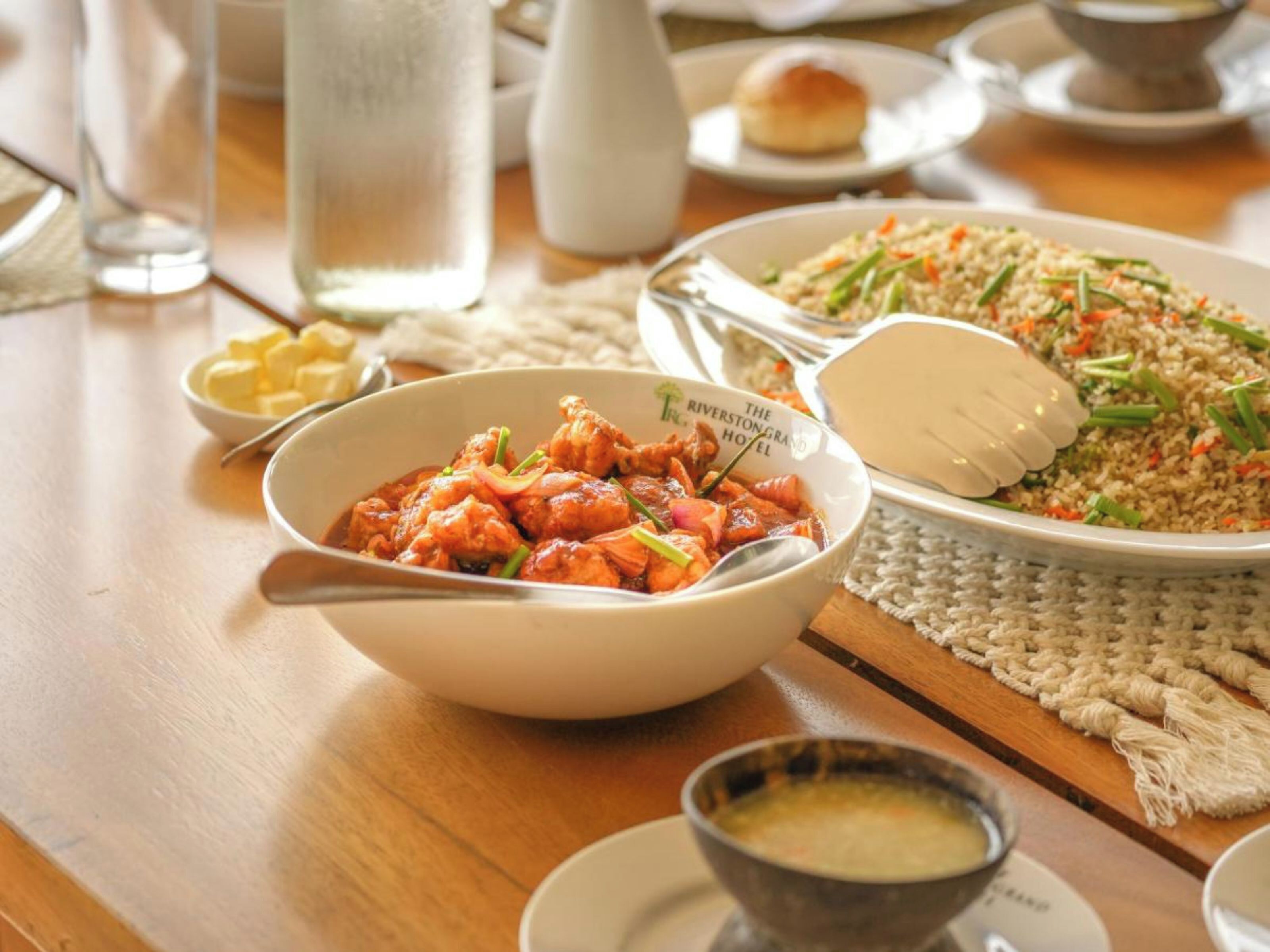 A dining table with a bowl of chicken, a plate of fried rice, and a small bowl of soup.