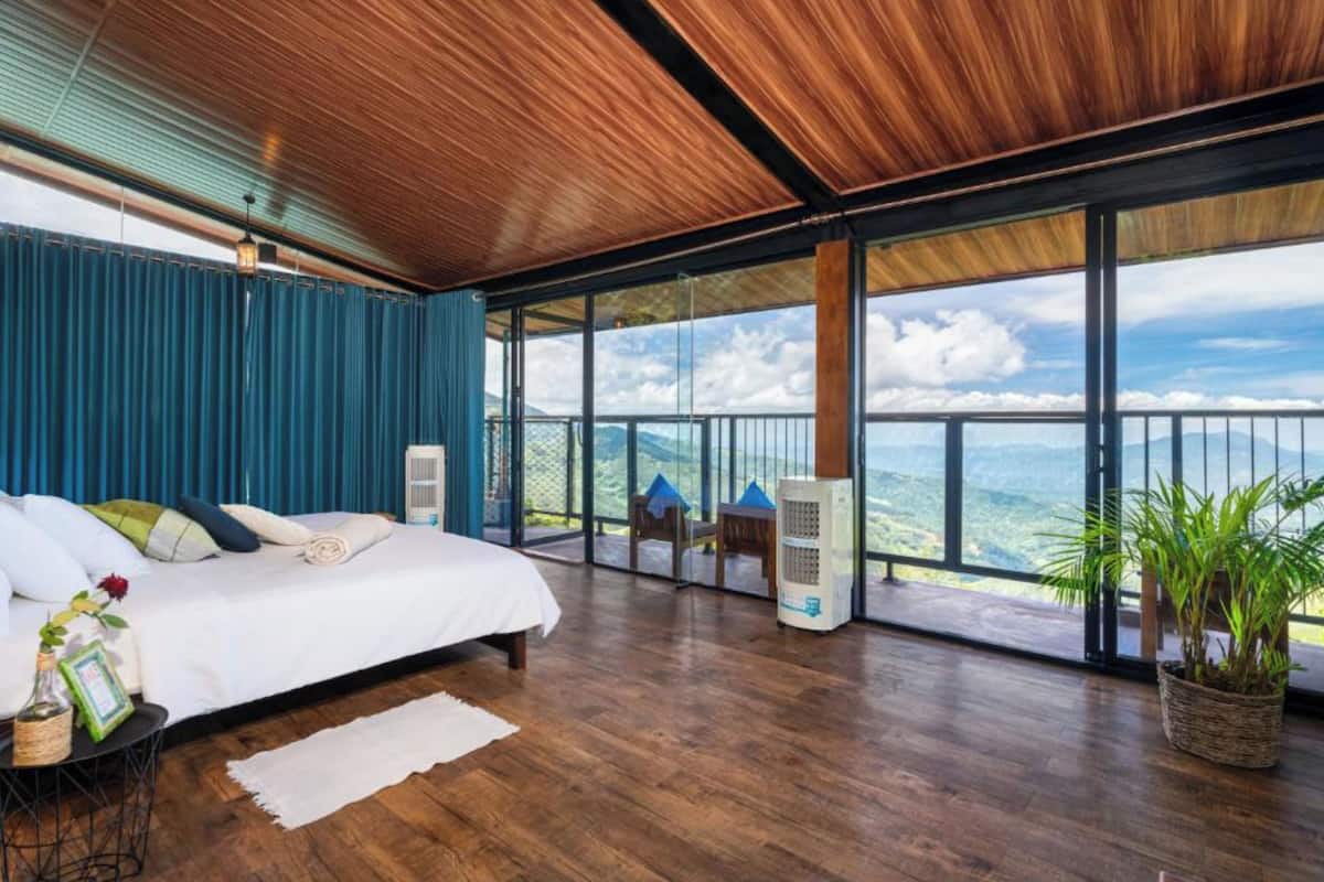 A bedroom with a large bed, a view of the mountains, and a balcony with a railing.