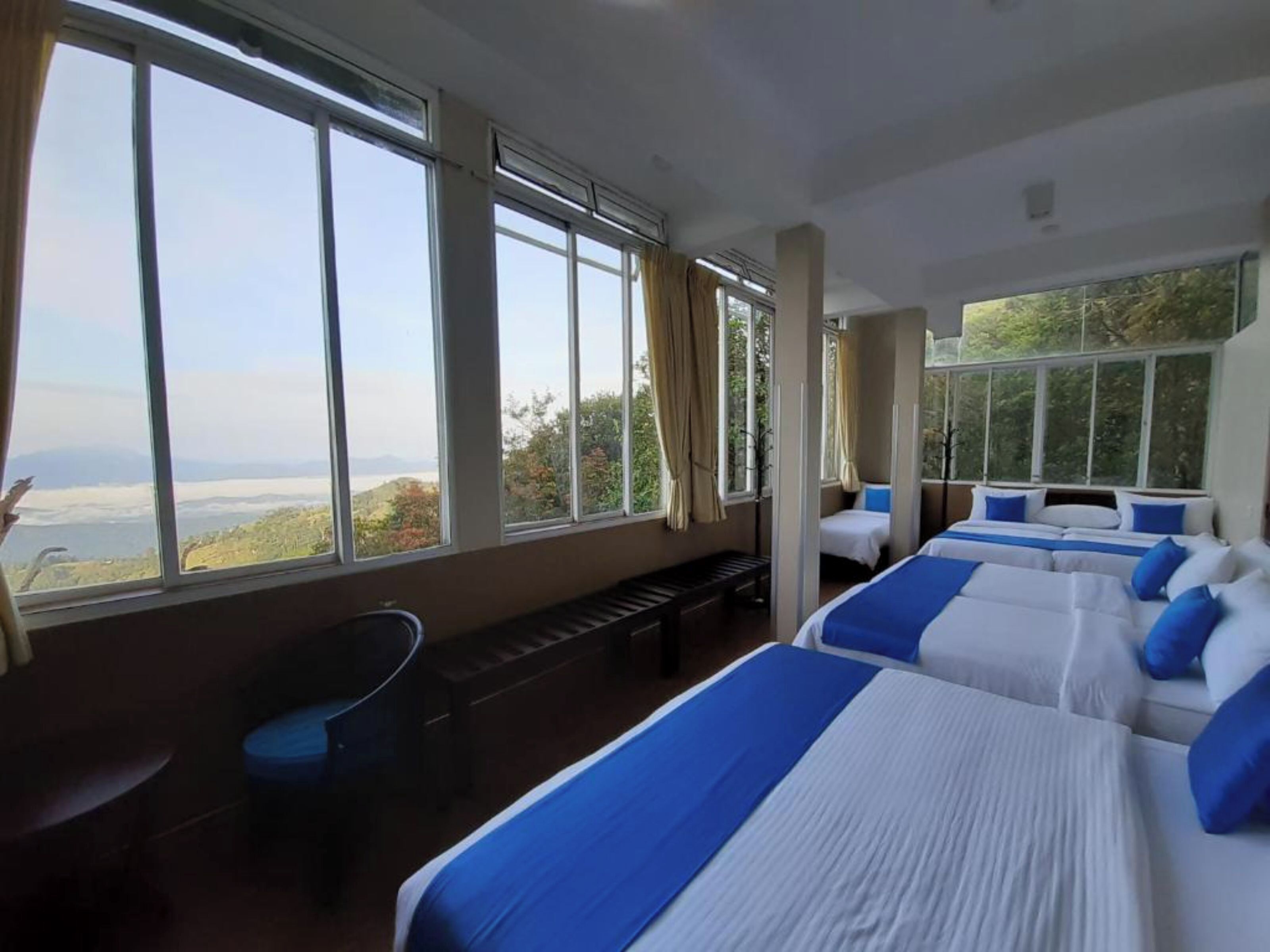 Ein Hotelzimmer mit großen Fenstern, zwei Betten, einer Bank und einem Sessel.