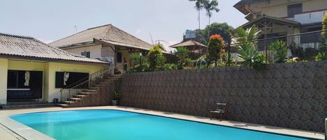 A swimming pool with steps leading into it, surrounded by a stone wall and a building with a tiled roof.