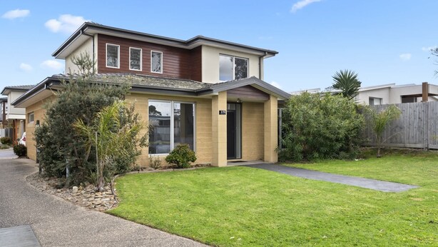 A two-story residential house with a front yard, a driveway, and a wooden fence.