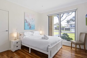 A bedroom with a bed, bedside tables, a chair, a window, and a painting.