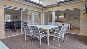 A spacious patio with a dining table and chairs, a foosball table, and a view of the kitchen and living area through glass doors.