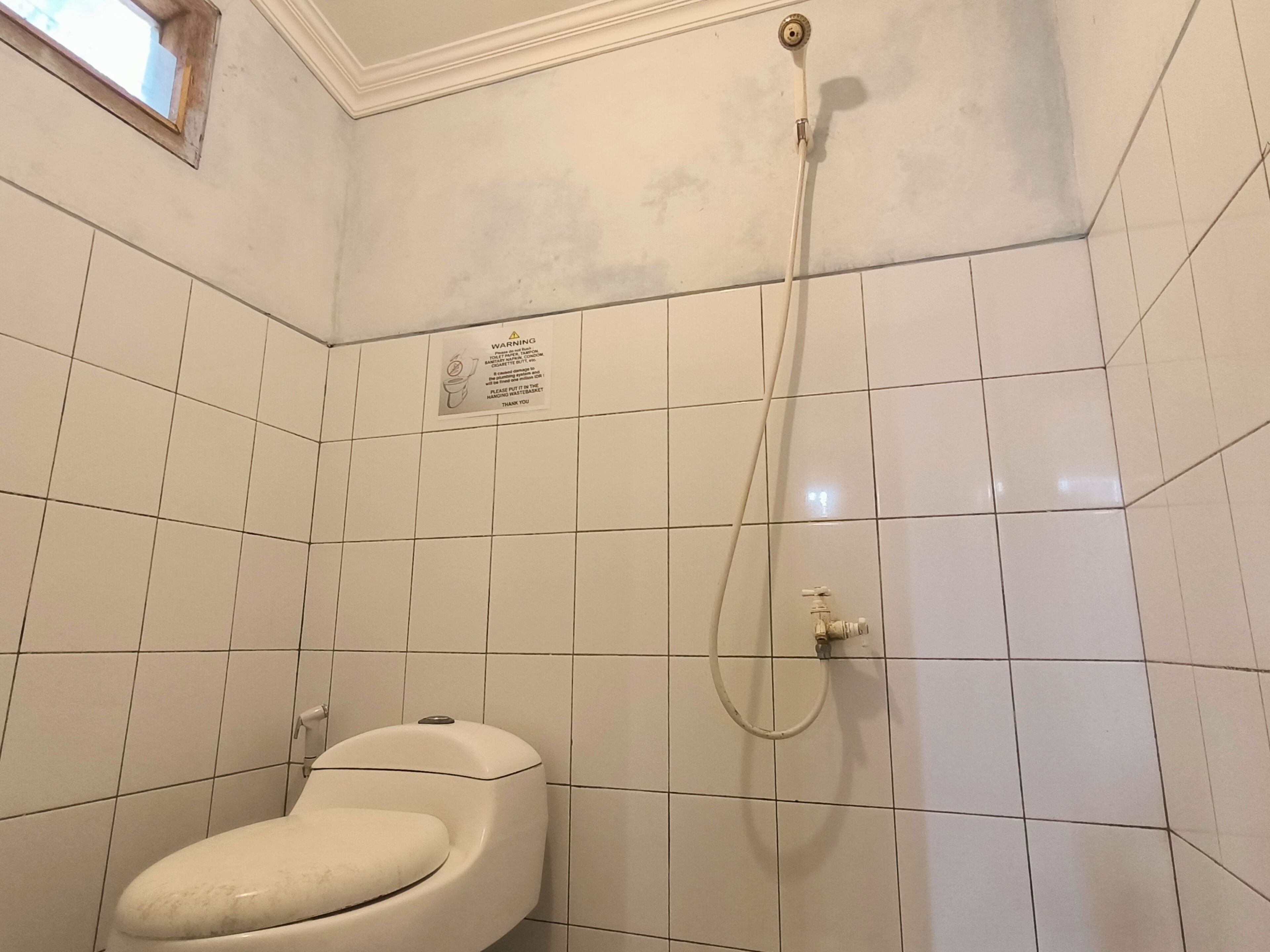 A bathroom with white tiled walls, a toilet, and a shower.