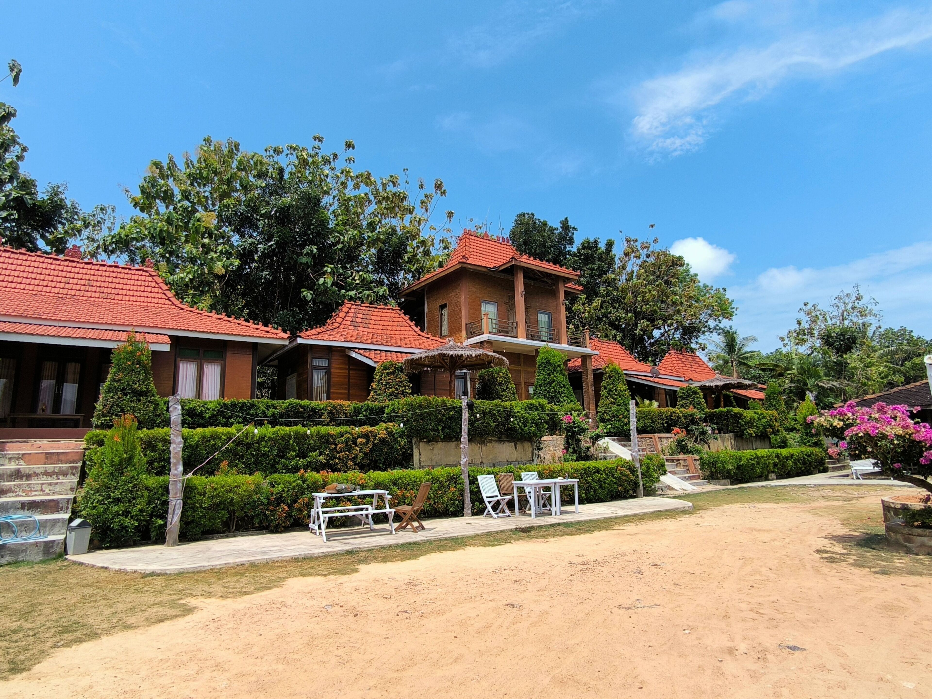 A resort with multiple buildings featuring red-tiled roofs, a well-maintained garden with various plants and flowers, and outdoor seating areas.