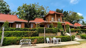 Un edificio de estilo bungalow con techo de tejas rojas, rodeado de exuberante vegetación y un jardín cuidado.