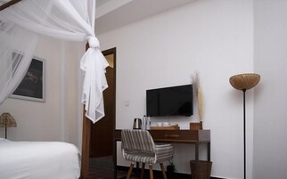 Un dormitorio con una cama, un escritorio con televisor, una silla, una mesita de noche y una lámpara de pie.