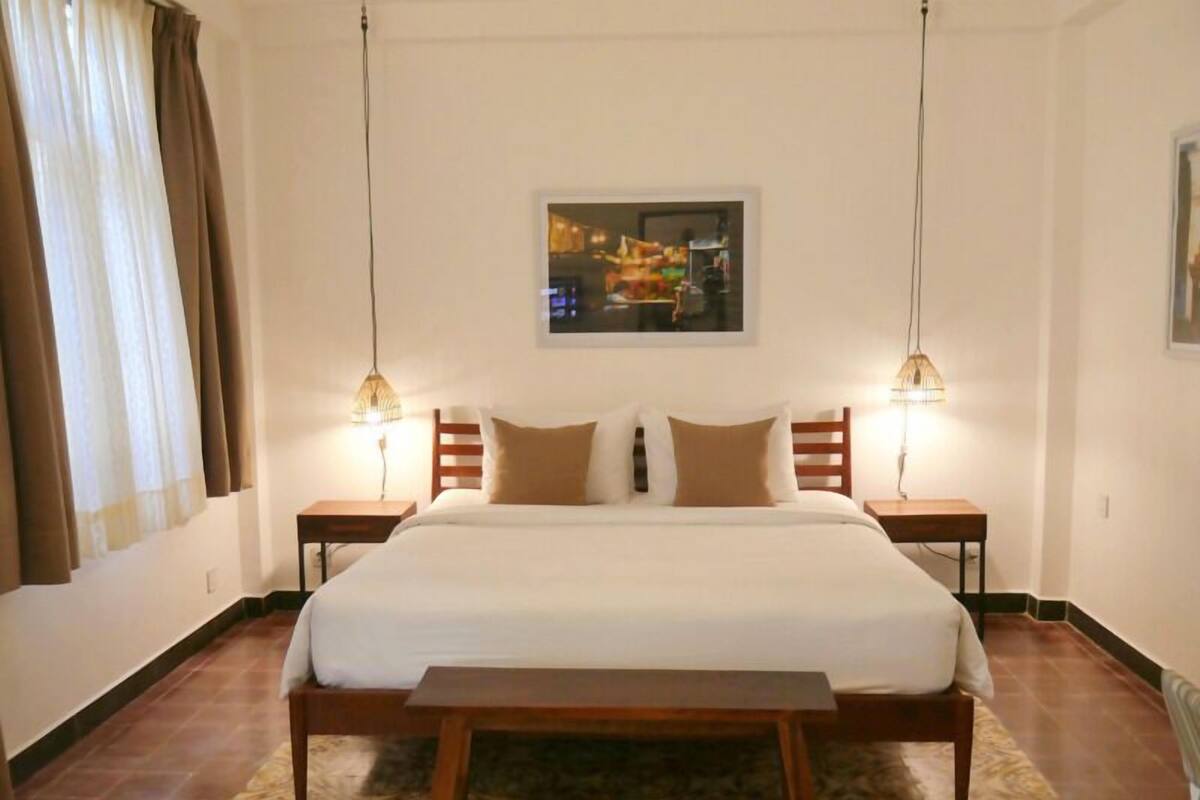 A neatly arranged hotel room with a large bed, two bedside tables, a small table, and a patterned rug.