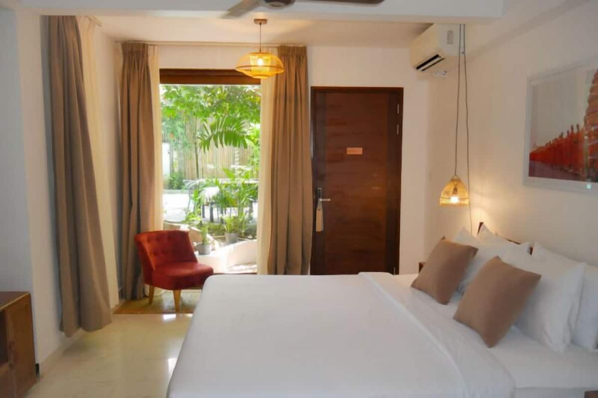 A hotel room with a large bed, a red armchair, and a view of a garden through a glass door.