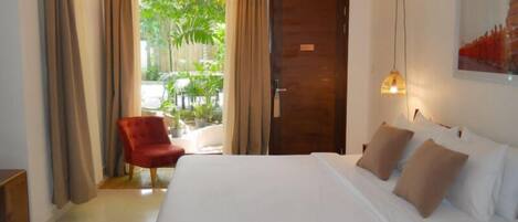 A hotel room with a large bed, a red armchair, and a view of a garden through a glass door.