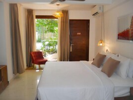 Habitación de hotel con una cama grande, un sillón rojo y vistas a un jardín a través de un ventanal.