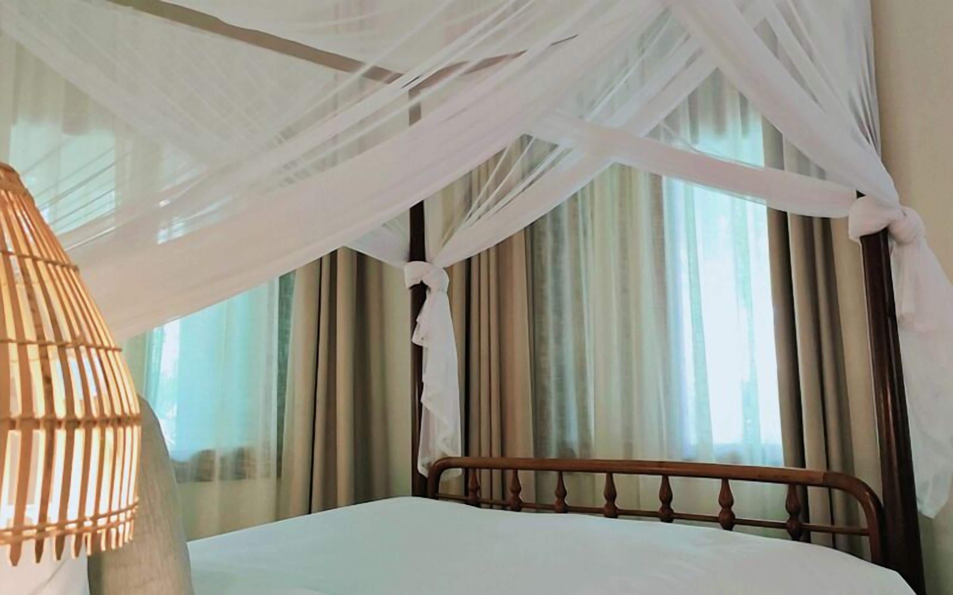 Una cama con cabecera de madera, ropa de cama blanca y un dosel con cortinas blancas.