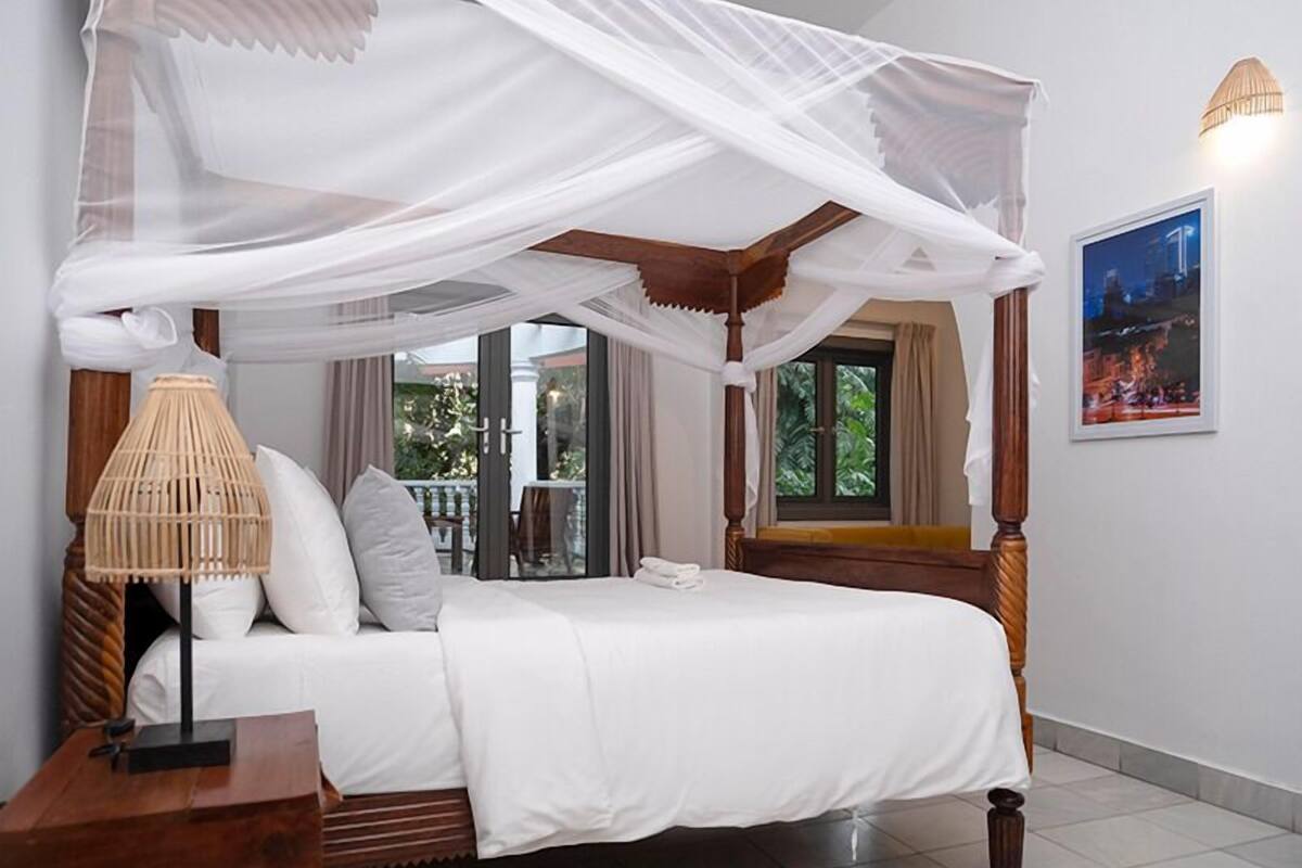 A four-poster bed with a canopy, white bedding, and a bedside table with a lamp.