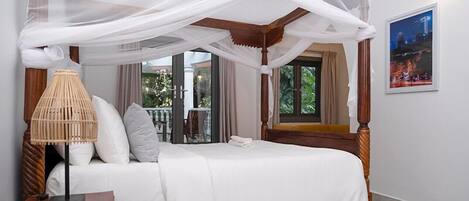 A four-poster bed with a canopy, white bedding, and a bedside table with a lamp.