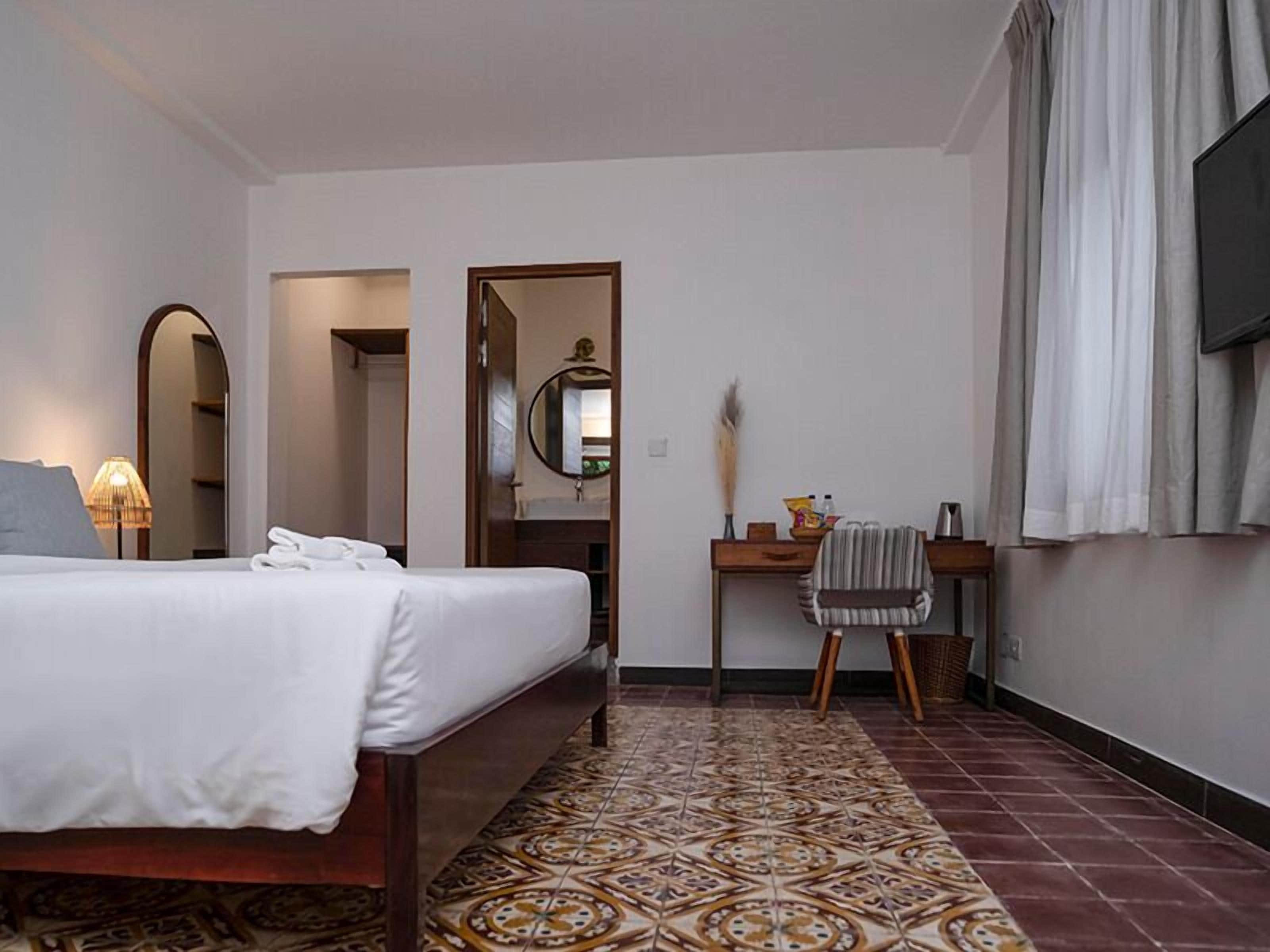 A hotel room with a bed, a desk, a mirror, and a TV.