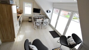 Une cuisine moderne avec des meubles blancs et un micro-ondes encastré, un coin repas avec une table et des chaises blanches, et de grandes fenêtres offrant une vue sur l’extérieur.